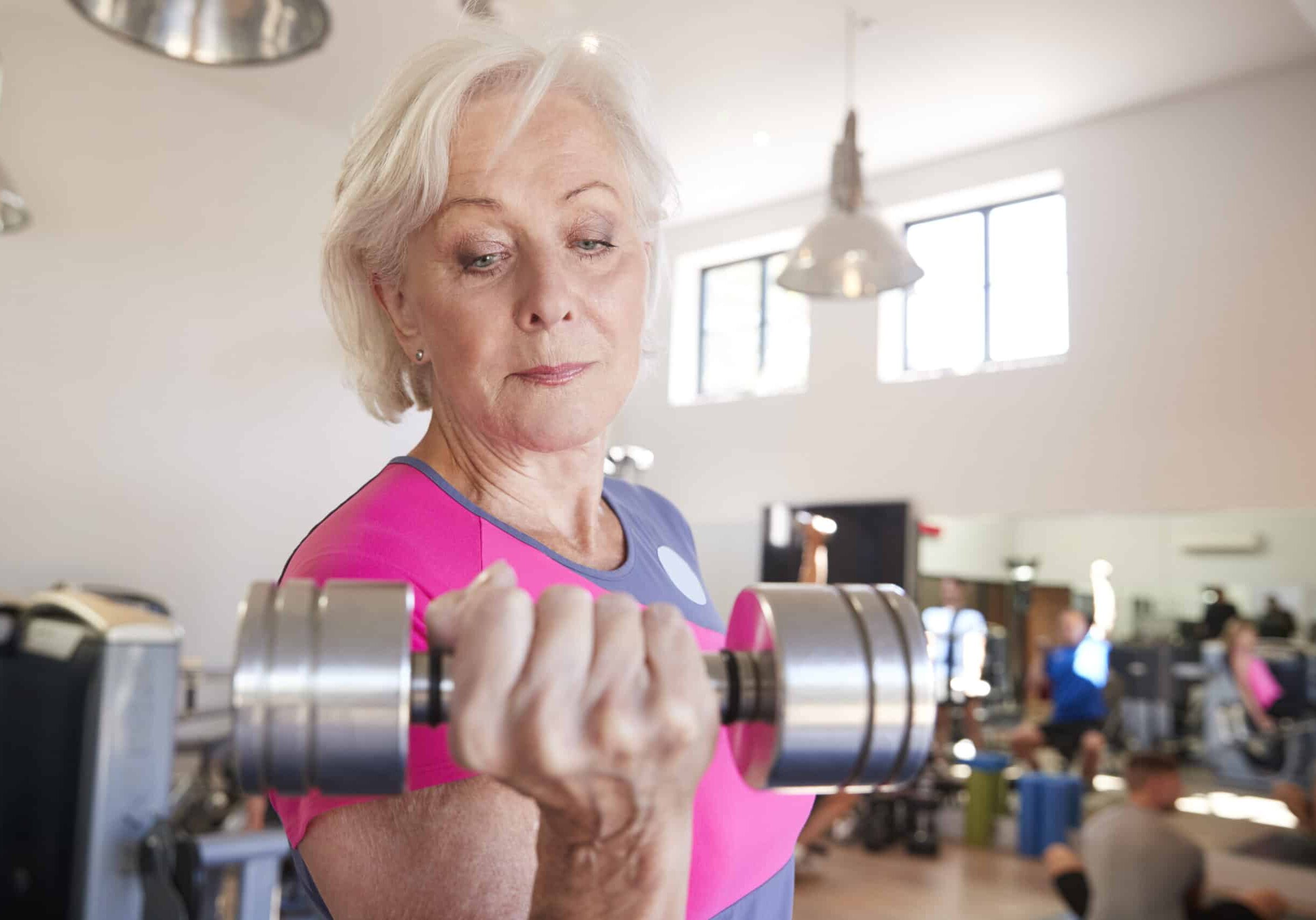 Senior Woman Exercising With Weights In Gym