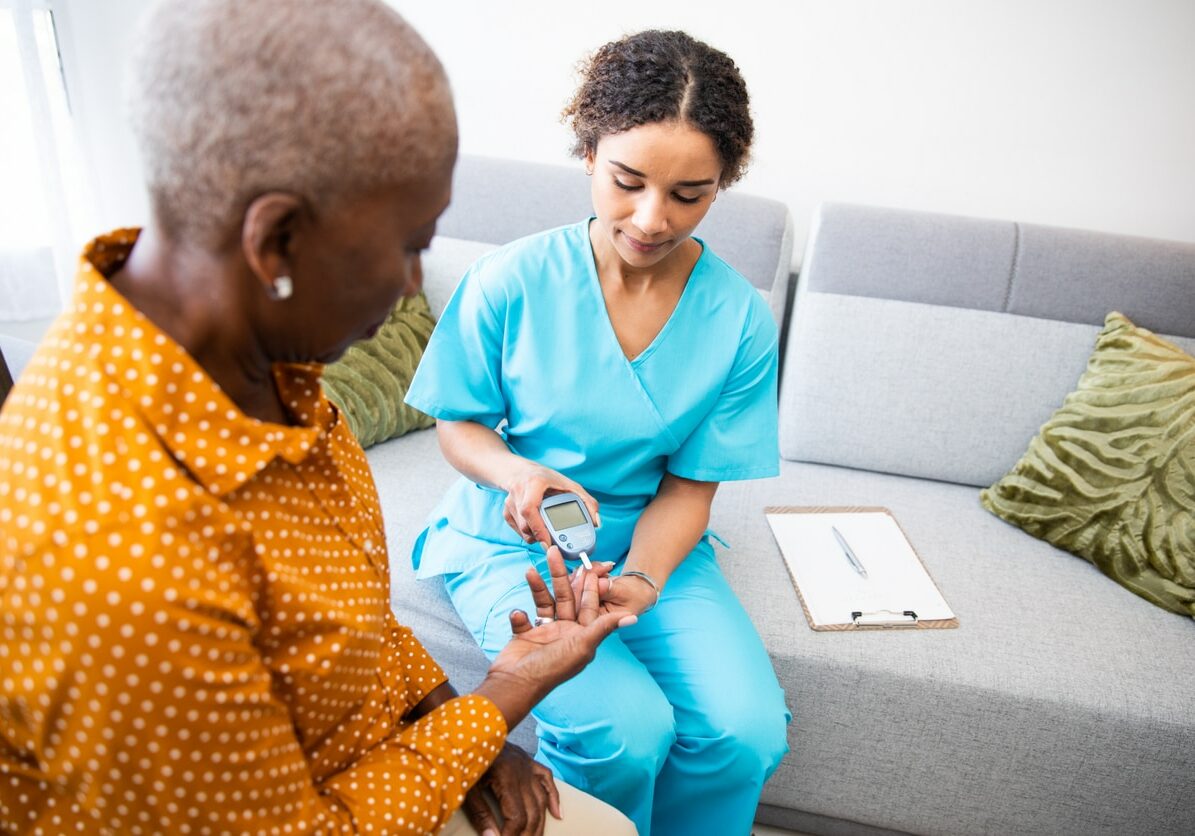 Young nurse doing a glucose blood test on her senior patient, during a home visit